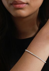 Bracciale d'argento con numerosi piccoli gemme trasparenti incastonati in una linea dritta. Indossato sul polso su uno sfondo di abbigliamento scuro.