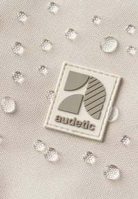 Világosszürke textúrájú anyag, amelyen kiemelkedő áttetsző vízcseppek találhatók, és a jobb alsó sarokban egy szürke és fehér téglalap alakú Audetic logó.
