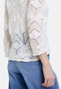Top bianco in maglia con un design testurizzato a foglia, maniche a tre quarti, abbinato a pantaloni in denim azzurro chiaro.
