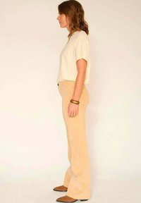 Haut beige à manches courtes associé à un pantalon en velours côtelé beige clair évasé. Bottes cheville marron, accessoirisées d'un bracelet et d'une bague.