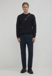 Marineblau gerippter Strickpullover, dunkelblaue Hose und schwarze Schnürschuhe, mit einer Umhängegurt-Accessoire, minimalistisches Design und strukturierte Passform.