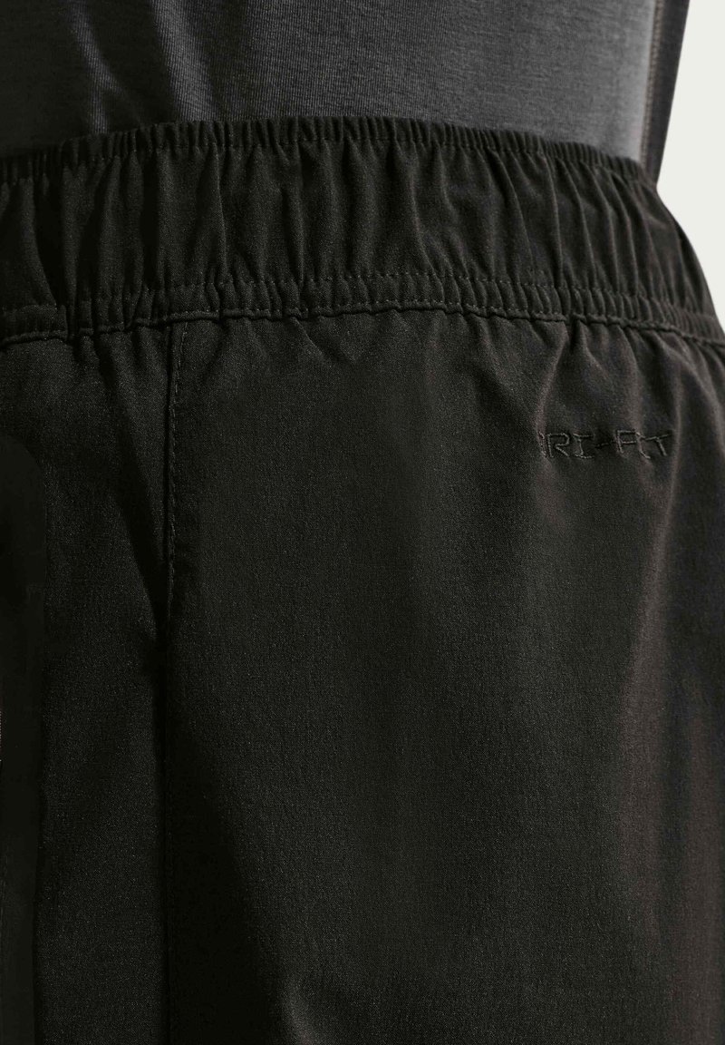 Dettaglio della fascia in vita di pantaloncini atletici neri con banda elastica e sottile scritta "DRI-FIT" ricamata sul tessuto.