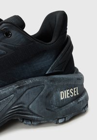 Close-up de sapatilhas Black Diesel, mostrando a sola texturizada, suporte acolchoado para o tornozelo e o nome da marca em relevo no calcanhar.