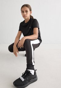 Crna atletska majica s logotipom, crne hlače s bijelim bočnim prugama i crne tenisice s istaknutim logotipom. Glatka tekstura.