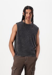 Sleeveless, dark grey cotton tank top with a relaxed fit, subtle distressing, and round neckline, paired with brown cargo pants featuring pockets.