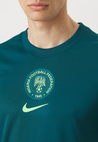 Camiseta deportiva verde de Nike con un logo circular de la Federación de Fútbol de Nigeria en verde claro y un pequeño logo Swoosh en verde claro.