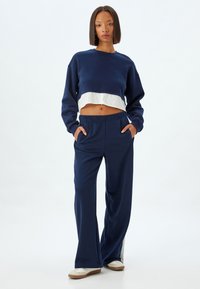 Marineblaues, verkürztes Sweatshirt mit weißem Saum, kombiniert mit marineblauen, weit geschnittenen Hosen mit seitlichen Taschen. Weicher Stoff mit lockerer Passform.