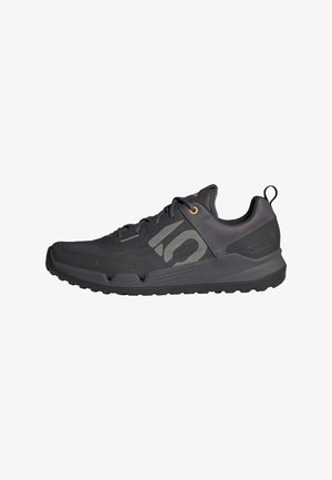Chaussure de sport noire avec une finition texturée, dotée d'un logo sur le côté, d'œillets dorés, d'une languette et d'une semelle en caoutchouc pour l'adhérence.