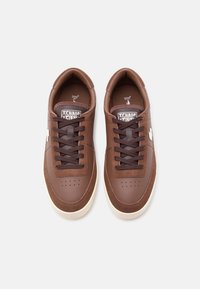 Ζευγάρι καφέ δερμάτινα και σουέντ αθλητικά παπούτσια με σκουρόχρωνα καφέ κορδόνια και λευκές καουτσούκ σόλες σε λευκό φόντο.