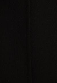 Tela negra con una textura suave y una costura vertical en el centro. Las puntadas son sutiles y del mismo color que la tela.