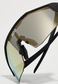 Sunglasses with a black frame, octagonal lenses featuring a gradient from brown to green, adjustable nose pads, and textured temples.