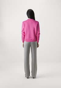Roze sweatshirt met lange mouwen, ronde halslijn en gebreide manchetten; gecombineerd met hoge taille, grijze, gebreide broek met wijde pijpen.