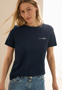 T-shirt en coton bleu marine à manches courtes, avec un texte brodé vert "il paradiso" sur la poitrine gauche. Coupe décontractée, texture lisse.