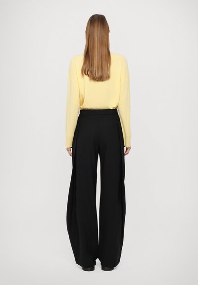 Suéter amarillo de corte holgado, combinado con pantalones anchos negros. La tela parece suave, con una textura lisa y un mínimo de detalles.
