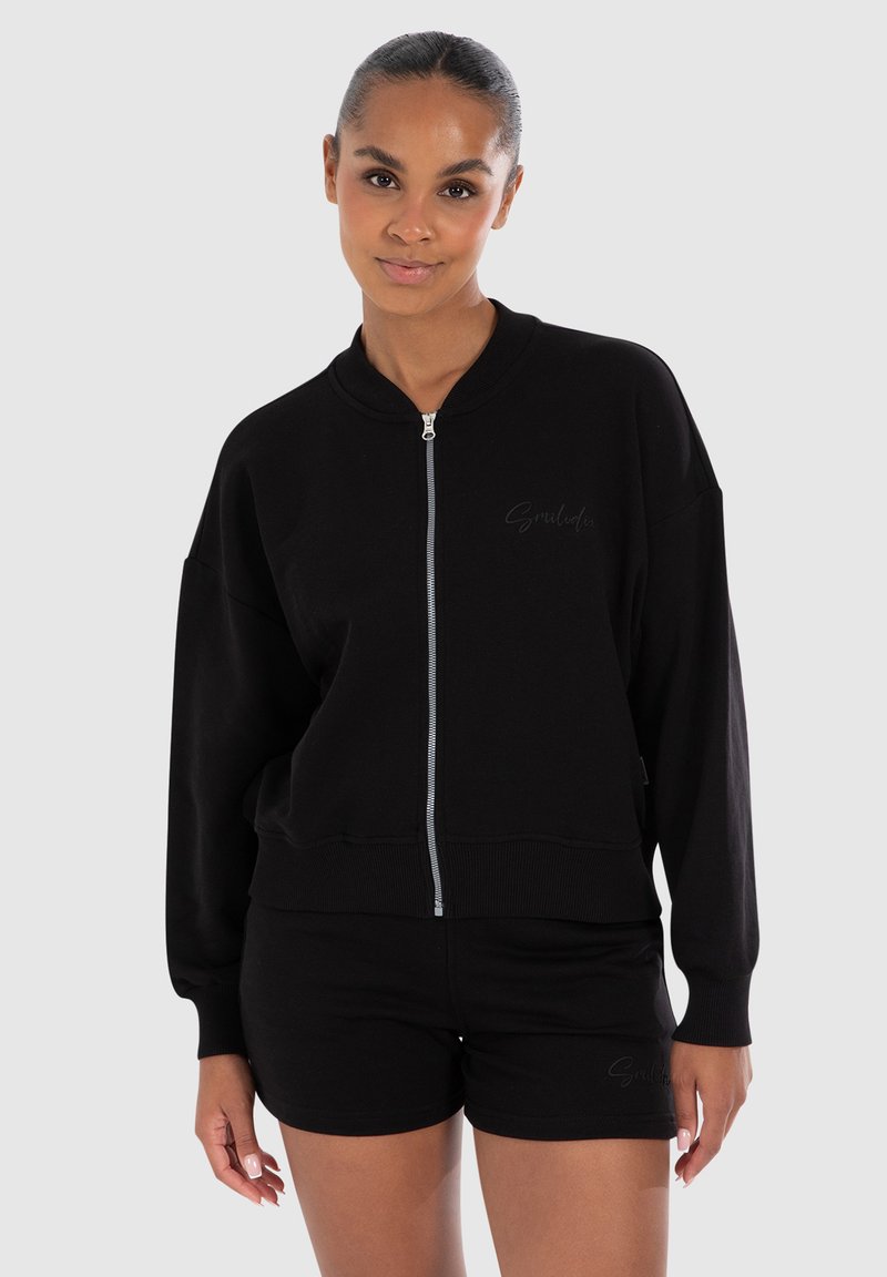Felpa nera con zip, dalla vestibilità oversize, con polsini e orlo a coste, e un sottile dettaglio con logo sulla parte anteriore, abbinata a pantaloni corti neri.