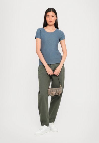 Blue ribbed short-sleeve top, green loose-fit pants, white sneakers, and a small gray handbag with gold hardware details.