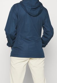 Granatowa, wodoodporna kurtka z kapturem, z długimi rękawami, zamkiem z przodu i eleganckim krojem. Charakterystyczna faktura z subtelnymi wzorami.