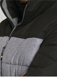 Veste matelassée avec un col haut. Présente des panneaux noirs et gris, une fermeture éclair et un cordon de serrage à l'ourlet. Texture douce.