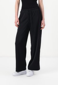 Sorte vide bukser laget av et lett, glatt stoff med elastisk midjebånd og snor, parret med hvite joggesko.
