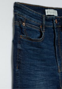 Jeans i mörkblå denim med orange sömmar, med en mid-rise midja, framfickor och en slät yta. Lappen synlig upptill.
