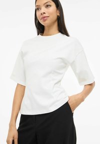 Biały top z krótkim rękawem wykonany z gładkiej bawełny, z okrągłym dekoltem i luźnym krojem. Noszony z czarnymi spodniami, podkreślający minimalistyczny design.