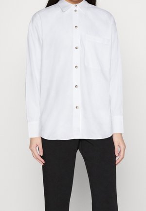 Biała, zapinana na guziki koszula z długim rękawem i kołnierzykiem, wyposażona w jedną kieszeń na piersi oraz guziki w srebrnym odcieniu. Gładka faktura materiału.