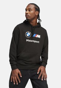 Black hoodie made of soft fabric, featuring a front pocket, drawstring hood, and graphics with BMW and M Motorsport logos in white and blue.