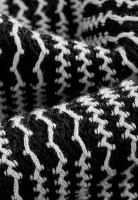 Textil con un patrón en blanco y negro de costuras en zigzag, tejido con hilos Texturizados, que exhibe un acabado suave y fibroso.