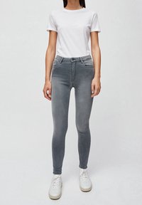 Vaqueros ajustados grises con una textura suave, cintura media y bolsillos frontales. Llevados con una camiseta blanca lisa y zapatillas blancas.