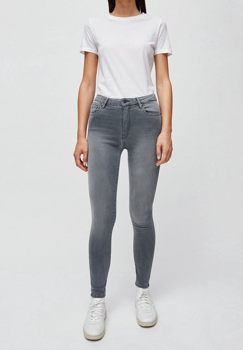 Vaqueros ajustados grises con una textura suave, cintura media y bolsillos frontales. Llevados con una camiseta blanca lisa y zapatillas blancas.