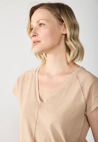 Beige V-neck short-sleeve t-shirt in soft fabric with visible seams and a relaxed fit, displayed against a neutral background.