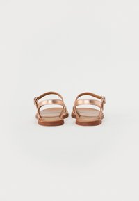 Sandaler i roségull metallisk farge med to tynne stropper, spenne-lukning og en brun flat såle. Glatt tekstur og minimalistisk design.