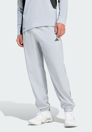 Light grey athletic pants with black accents, crafted from breathable fabric featuring a tapered fit and elastic cuffs, paired with white sneakers.
