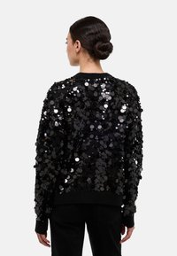 Pull noir couvert de grandes paillettes brillantes, avec un col rond et des poignets côtelés, doté d'une coupe décontractée et d'un ourlet uni noir.