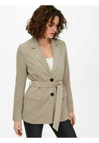Blazer di velluto a coste beige con colletto a revers, vita con cintura, due tasche frontali e bottoni neri. Presenta una texture a coste verticali.