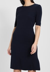 Marinblå klänning i stretchmaterial, med rundad halsringning, korta ärmar och en figurnära byst som flarear något vid fållen.
