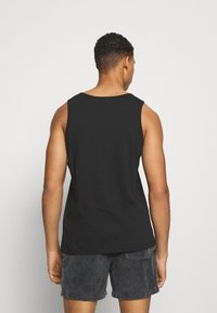 Sort ærmeløs tanktop med rund halsudskæring, lavet af blødt bomuld. Har en glat tekstur og en løs pasform, parret med grå shorts.
