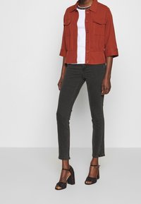 Rusti-värinen lyhyt takki, jossa on etutaskut, päällä valkoinen paita ja yhdistetty tummiin skinny-farkkuihin sekä ruudullisiin korkokenkiin.