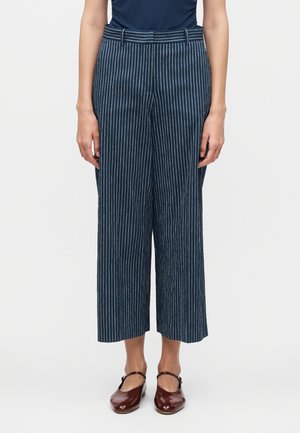 Personne portant un pantalon large court bleu marine avec des rayures verticales blanches et des chaussures Mary Jane rouge foncé.