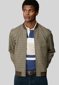 Brown checkered bomber jacket with a ribbed collar and cuffs, featuring leather accents. Worn over a striped polo shirt.