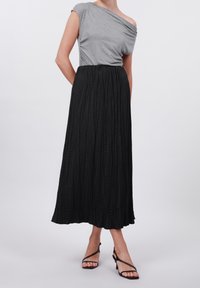 Black pleated maxi skirt with a textured design, paired with a grey off-shoulder top and black strappy sandals. Casual outfit display.