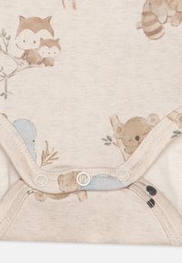Kortermet baby bodysuit laget av lys beige bomull. Har et lekent dyremønster med ugler, koalaer og vaskebjørner. Trykknapper nederst.