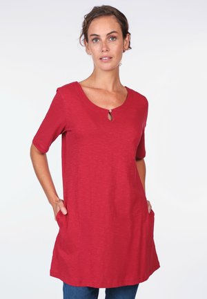 Red tunic top with short sleeves and round neckline featuring a keyhole detail. Made of soft fabric, it has two side pockets.