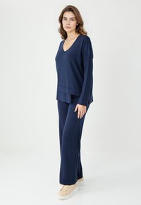 Marine loungewear set omvat een V-hals langemouwen top met een gelaagde zoom en bijpassende wijde pijpen, gemaakt van zachte, gestructureerde stof.
