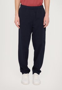 Marinblå sweatpants med elastisk midja, sidofickor och texturerade detaljer på benen. Tillverkade av mjukt, andningsbart material.