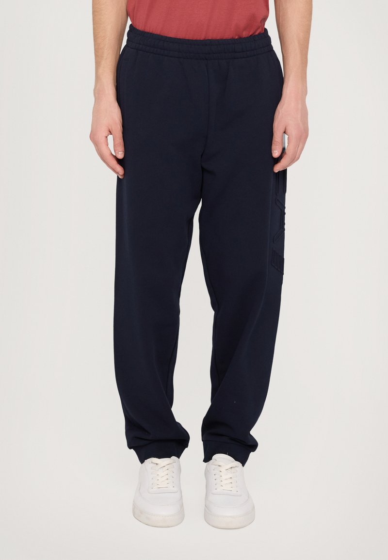 Marinblå sweatpants med elastisk midja, sidofickor och texturerade detaljer på benen. Tillverkade av mjukt, andningsbart material.