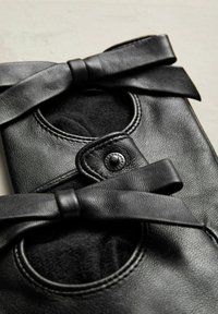 Schwarze Leder-Schuhe mit runden Öffnungen, die mit großen Schleifen verziert sind. Sie haben eine glatte Textur und kreisförmige Stickdetails.