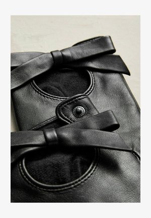 Melnas ādas kurpes ar noapaļotām atverēm, pabeigtas ar lielām lentēm. Raksturīga gluda faktūra un apaļas šuvju akcenti.