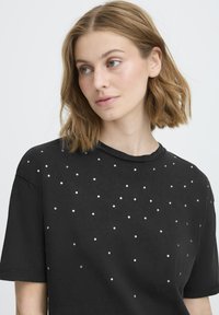 Sort T-shirt lavet af blødt stof med en afslappet pasform, med spredte sølvnitter, der skaber et tekstureret mønster på forsiden.