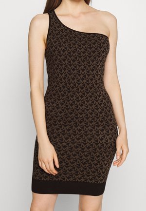 Robe noire ajustée asymétrique avec motif géométrique marron, portée par une femme debout devant un fond clair uni.
